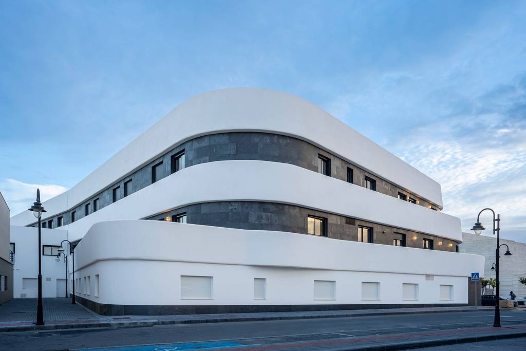 Fachada blanca de líneas curvas y piedra oscura de una residencia de mayores al atardecer