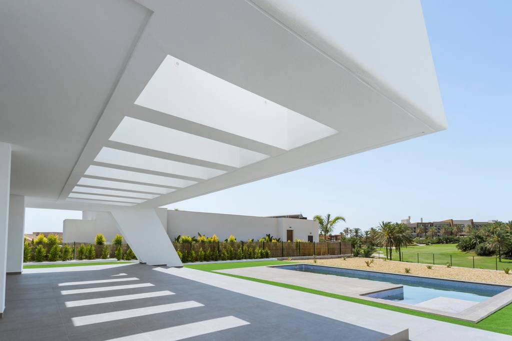 Porche blanco con pérgola y franjas de luz junto a la piscina de una vivienda unifamiliar